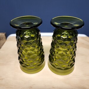May include: Two matching olive green glass tumblers featuring a textured, geometric diamond pattern across the exterior. Each glass has a wide, smooth circular base and a slightly flared, smooth rim, showcasing a translucent finish throughout.