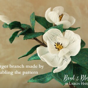 May include: A close-up of a beaded magnolia flower branch with green leaves. The branch is made by doubling the pattern. The text "Bead & Blossom by Lauren Harpster" is visible in the bottom right corner of the image.
