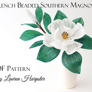 May include: A white beaded Southern Magnolia flower with green leaves in a white vase. The flower is made with white beads and the leaves are made with green beads. The flower is in a white vase. The image includes the text "French Beaded Southern Magnolia" and "PDF Pattern By Lauren Harpster".