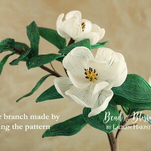 May include: A beaded magnolia flower branch with white blossoms and green leaves. The branch is made by doubling the pattern. The text "Bead & Blossom by Lauren Harpster" is visible in the image.