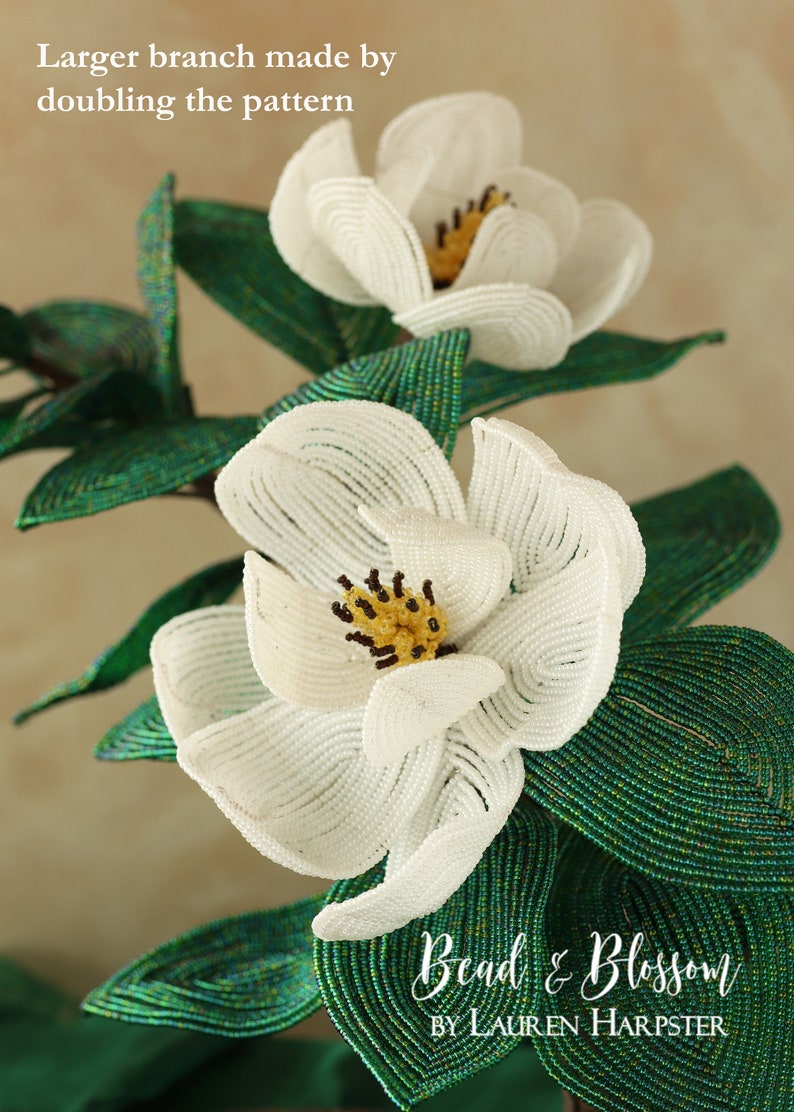 May include: A close-up of a white beaded magnolia flower with a yellow center. The flower is part of a larger beaded floral arrangement with green leaves. The text "Bead & Blossom by Lauren Harpster" is visible in the bottom right corner of the image.
