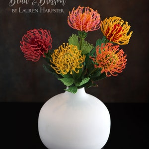 May include: A bouquet of beaded flowers in a white vase. The flowers are red, orange, and yellow and have a spiky, pinecone-like shape. The text "Bead & Blossom BY LAUREN HARPSTER" is visible at the top of the image.
