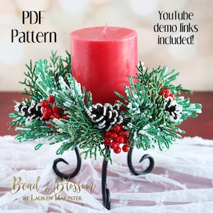 Puede incluir: Un anillo de vela de Navidad de cuentas con ramas de pino verdes y blancas, bayas rojas y piñas. El anillo está en un portavelas de metal negro. El texto "PDF Pattern" y "YouTube demo links included!" está en la imagen.