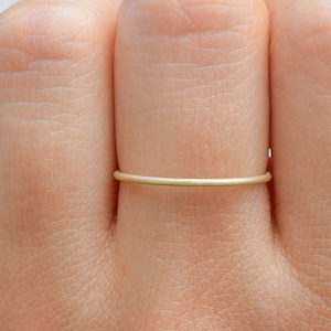 May include: A simple gold band ring worn on a finger.