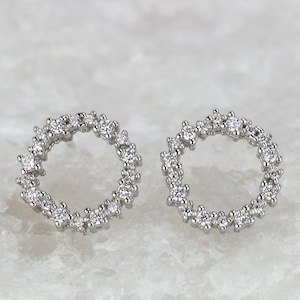May include: A pair of silver stud earrings with a circle design. The circle is made of small, clear stones.