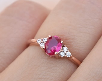 Può includere: Un anello in oro rosa con una pietra ovale rossa circondata da piccole pietre trasparenti.