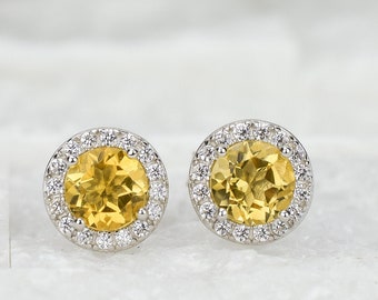 May include: A pair of gold and white round stud earrings with a halo of small diamonds surrounding a larger yellow gemstone in the center.