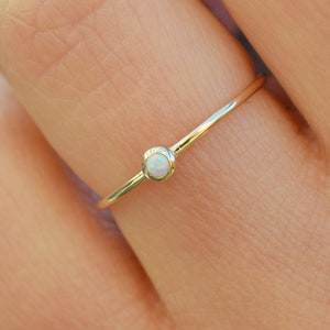 Könnte beinhalten: Ein zarter Goldring mit einem kleinen weißen Opal-Edelstein.