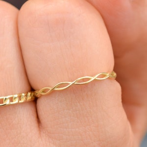 Könnte beinhalten: Ein goldfarbener Ring mit einem gedrehten Design. Der Ring wird an einem Finger getragen.