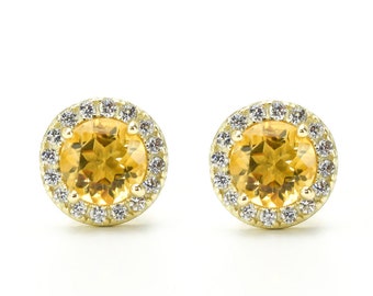 May include: A pair of gold earrings with a round, yellow gemstone surrounded by a halo of smaller, white gemstones.