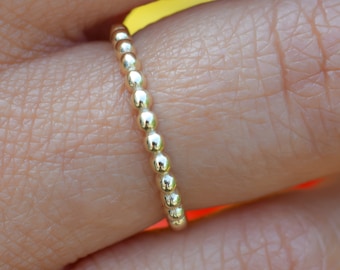 Könnte beinhalten: Ein zarter goldener Perlenring, der an einem Finger getragen wird.