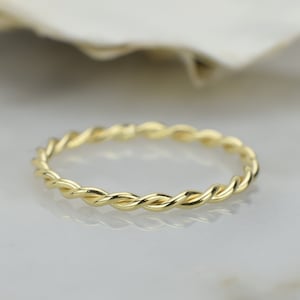 Könnte beinhalten: Ein einfacher goldener Ring mit einem gedrehten Design.