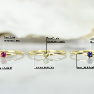 May include: Three gold rings with different colored gemstones. The rings are 1mm thick and made of 14k solid gold. The gemstones are 2mm in diameter and are ruby, peridot, and sapphire. The text below each ring reads "2mm Ruby Birthstone: July", "2mm Peridot Birthstone: August", and "2mm Sapphire Birthstone: September".