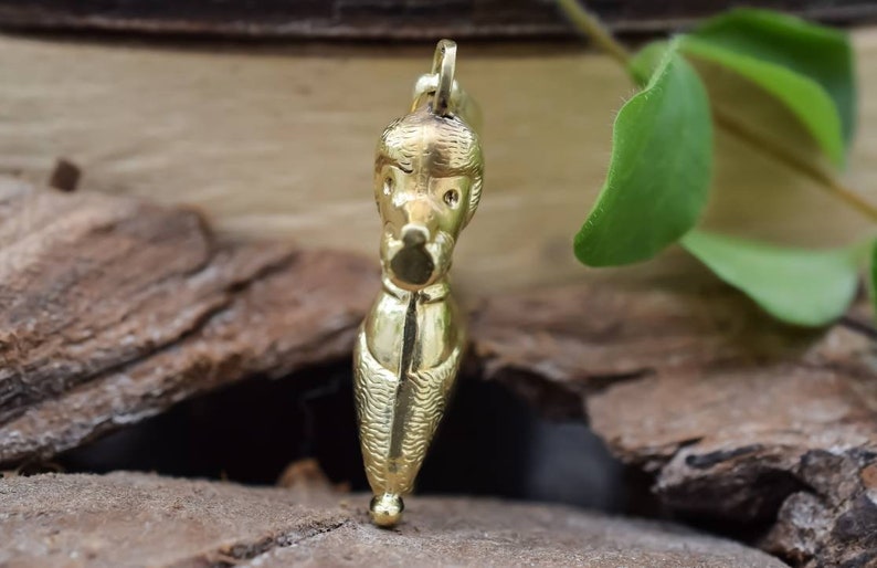 Puede incluir: Un colgante de color dorado con forma de caniche, sobre una superficie de madera.