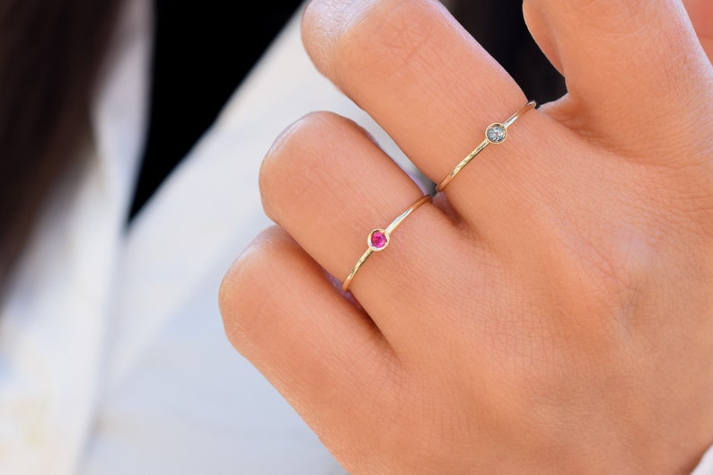 May include: Two delicate gold rings with small gemstones. One ring has a red gemstone and the other has a clear gemstone.