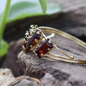 May include: A gold bangle bracelet with three rectangular brown gemstones. The bracelet is on a wooden surface.