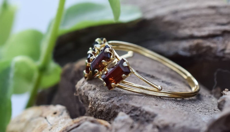 May include: A gold bangle bracelet with three rectangular brown gemstones. The bracelet is on a wooden surface.