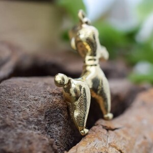 Puede incluir: Un colgante de caniche de color dorado. El caniche est&aacute; de pie sobre sus patas traseras con la cola enroscada. El colgante est&aacute; detallado con pelo texturizado y un peque&ntilde;o collar.