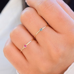 May include: Two delicate gold rings with small gemstones. One ring has a red gemstone and the other has a blue gemstone.