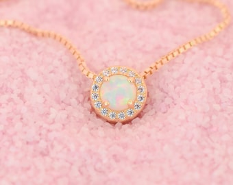 Puede incluir: Un delicado collar de oro con un colgante redondo de ópalo rodeado por un halo de piedras pequeñas transparentes.