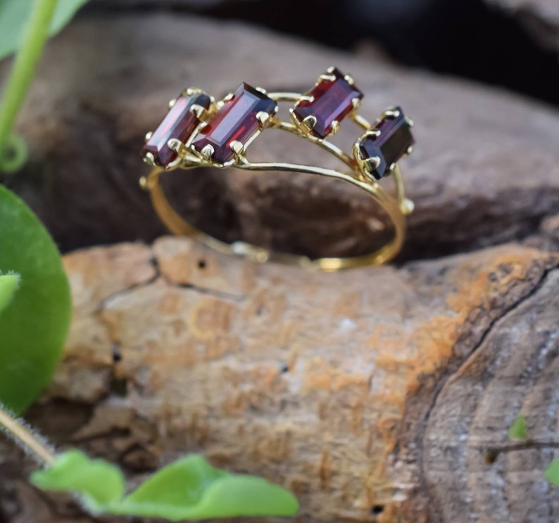 May include: A gold ring with five red rectangular gemstones set in a delicate, twisted band.