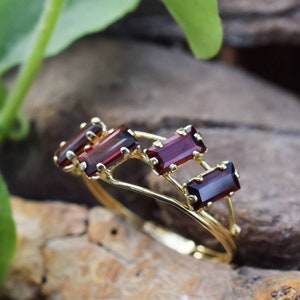 May include: A gold ring with four rectangular red gemstones set in a delicate, interwoven design.