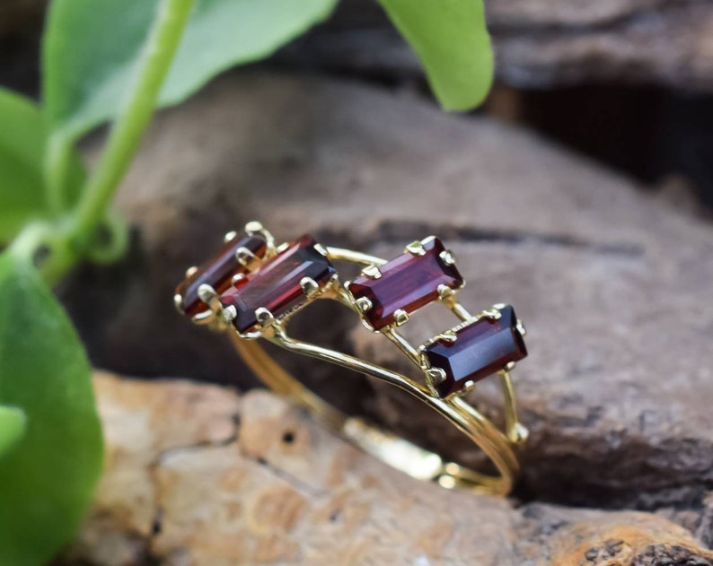May include: A gold ring with four rectangular red gemstones set in a delicate, interwoven design.