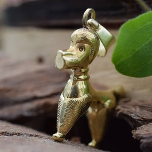Puede incluir: Un colgante de caniche de color dorado. El caniche est&aacute; de pie sobre sus cuatro patas con la cabeza inclinada hacia un lado. El colgante tiene un dise&ntilde;o detallado y un acabado brillante.