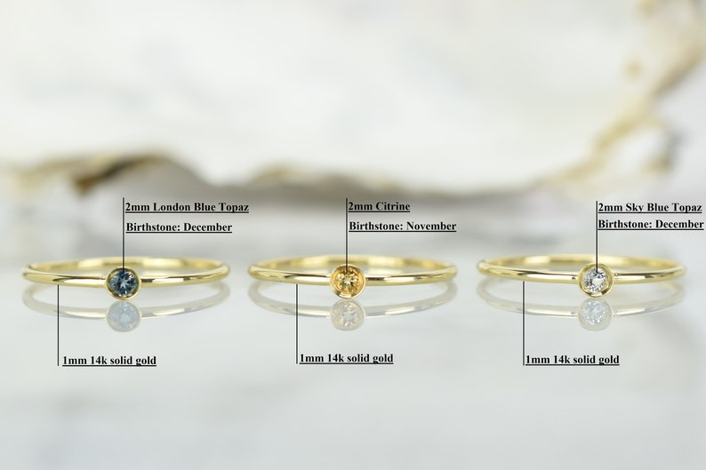 May include: Three gold rings with different colored gemstones. The rings are 1 mm wide and made of 14k solid gold. The gemstones are 2 mm in diameter. The first ring has a blue topaz, the second ring has a citrine, and the third ring has a sky blue topaz.