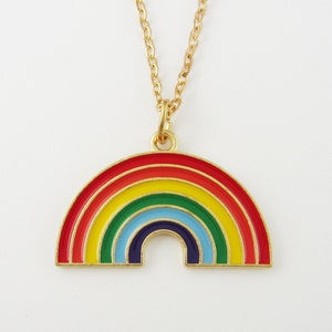 May include: A gold-toned metal necklace featuring a semi-circular rainbow pendant. The pendant is filled with enamel stripes in red, orange, yellow, green, light blue, and dark blue. The pendant hangs from a matching gold-toned metal chain link.
