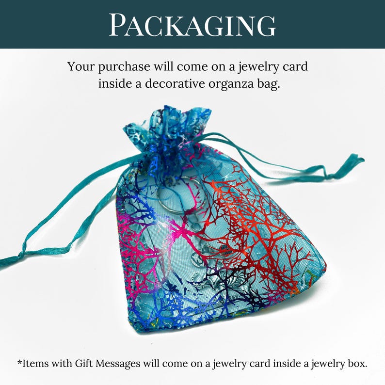 May include: A translucent organza drawstring bag featuring a vibrant blue, purple, and red coral-like pattern. The bag contains a jewellery card and a metallic item. Text reads: PACKAGING, Your purchase will come on a jewellery card inside a decorative organza bag, and *Items with Gift Messages will come on a jewellery card inside a jewellery box.