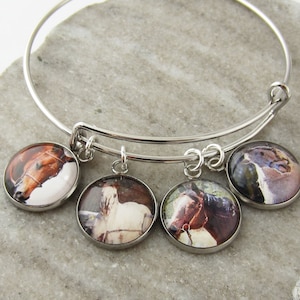 May include: A silver-toned metal bangle bracelet featuring four circular charms. Each charm displays a different photographic image of a horse, including brown and white coat colours, set under a clear, rounded glass cabochon dome.