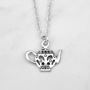 May include: A silver-colored pendant necklace featuring a detailed teapot charm. The teapot has a handle, spout, and decorative cutouts. The necklace chain is delicate and silver, creating a simple yet elegant accessory.