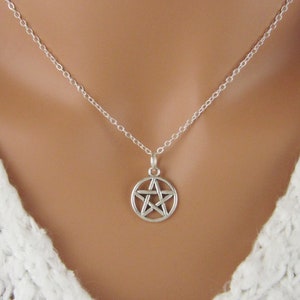 May include: A silver-coloured necklace featuring a circular pendant with a five-pointed star pentagram design. The pendant hangs from a delicate, thin silver-coloured chain with small, uniform circular links that connect to the top of the charm.