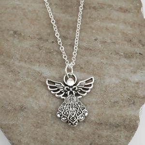 May include: A silver-toned metal angel pendant necklace featuring an intricate filigree design on the wings and dress. The pendant is suspended from a simple silver-toned link chain, showcasing a detailed cutout pattern throughout the figure.