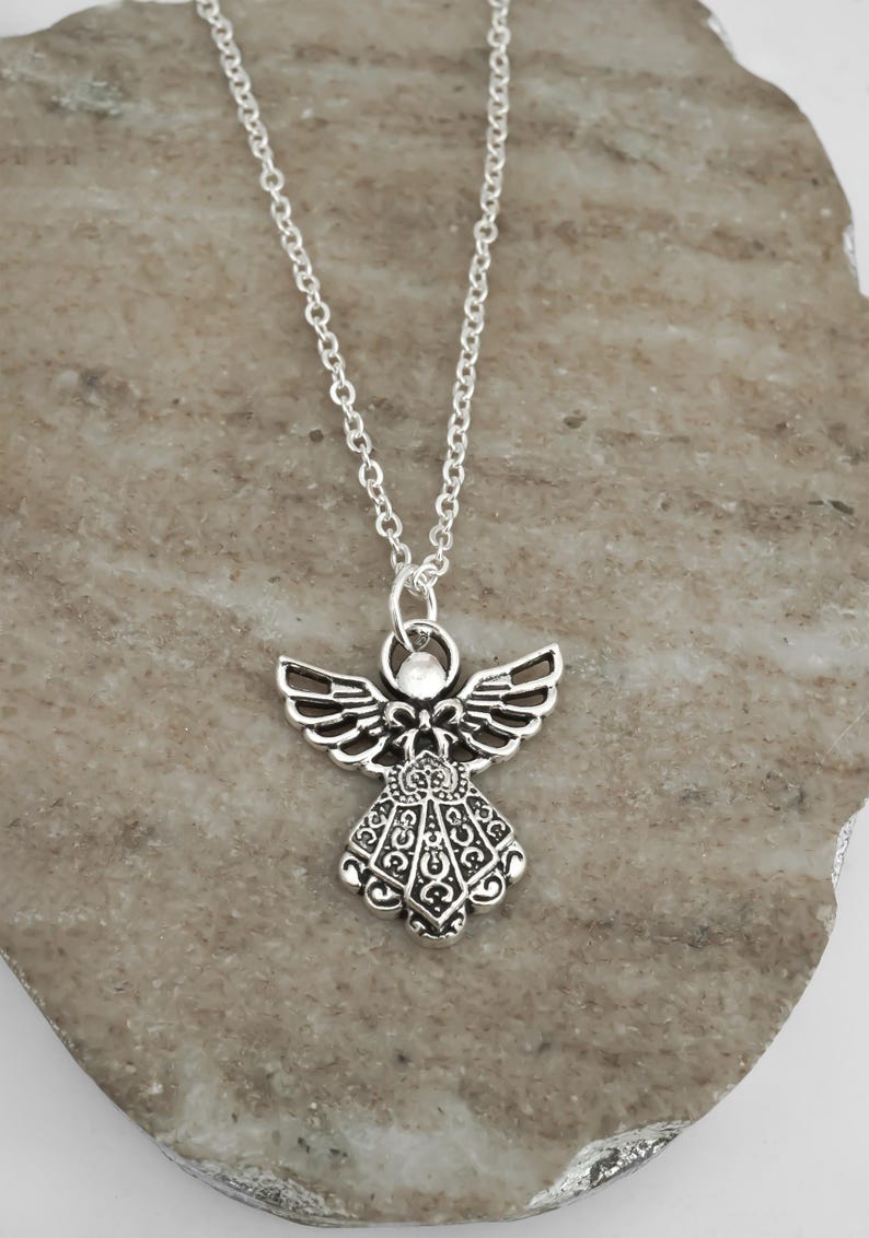 May include: A silver-toned metal angel pendant necklace featuring an intricate filigree design on the wings and dress. The pendant is suspended from a simple silver-toned link chain, showcasing a detailed cutout pattern throughout the figure.