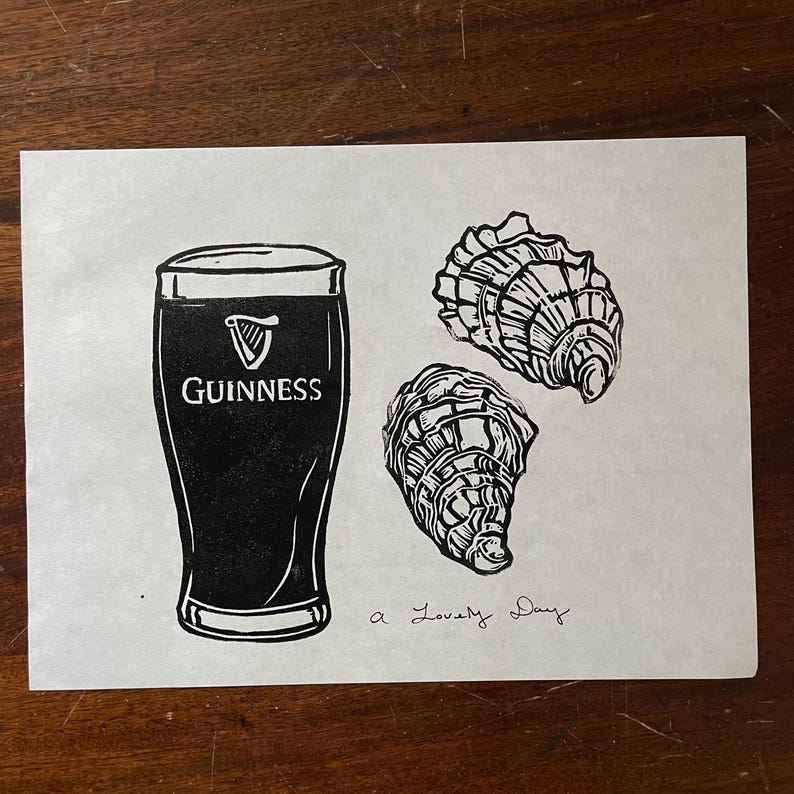 Pu&ograve; includere: Una stampa in linoleum in bianco e nero di un bicchiere di birra Guinness e tre ostriche. Il testo "a lovely day" &egrave; scritto sotto l'immagine.