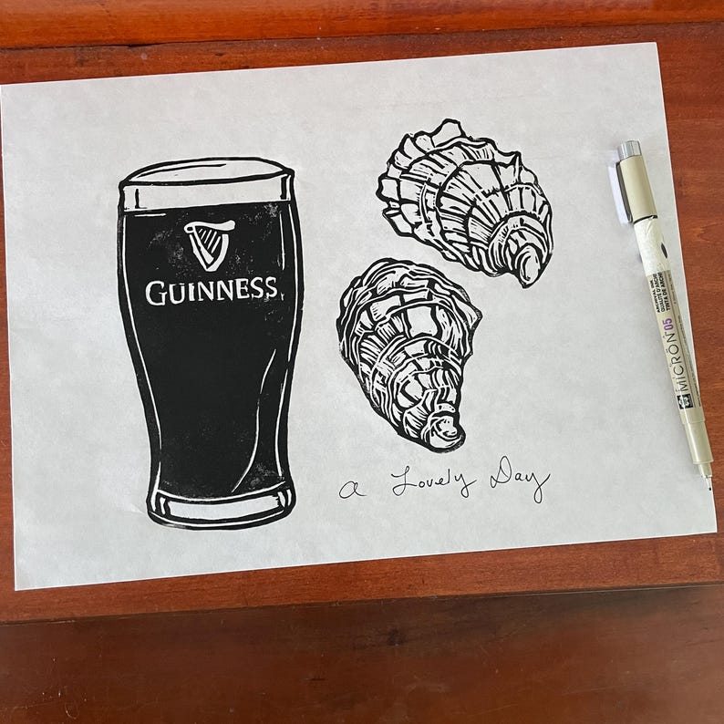 Pu&ograve; includere: Un'illustrazione in bianco e nero di una pinta di birra Guinness e due ostriche. Il testo "a lovely day" &egrave; scritto sotto l'immagine.