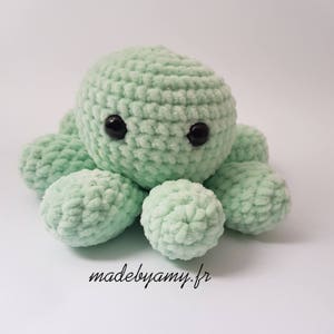 Puede incluir: Un pulpo de crochet suave y verde con ojos negros. El pulpo está hecho con un hilo peludo y tiene ocho tentáculos.
