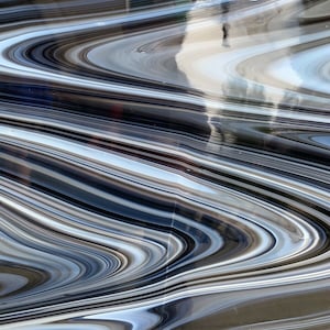 May include: Abstract image with a flowing pattern of swirling lines in shades of gray, black, and white. The design has a glossy, reflective surface, creating a sense of depth and movement. The pattern resembles a liquid or marbled effect.