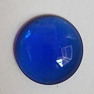May include: A round, blue glass cabochon with a smooth, shiny surface.