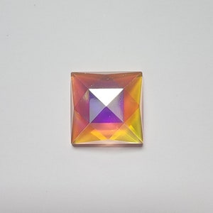 May include: A square iridescent gemstone with a pyramid shape. The gemstone is a mix of yellow, orange, and purple.