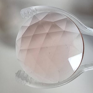 May include: A pink faceted gemstone held in a clear plastic clamp.