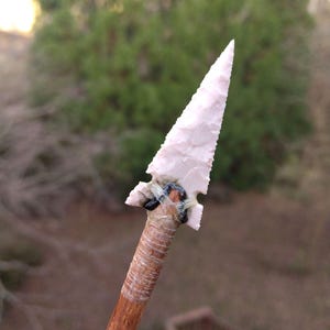 May include: A pink arrowhead attached to a wooden shaft with black tape.