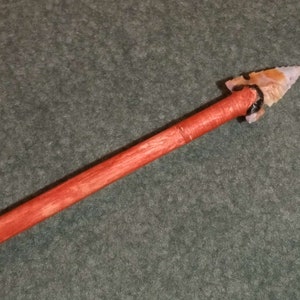 May include: A wooden arrow with a red stain and a brown and white arrowhead.