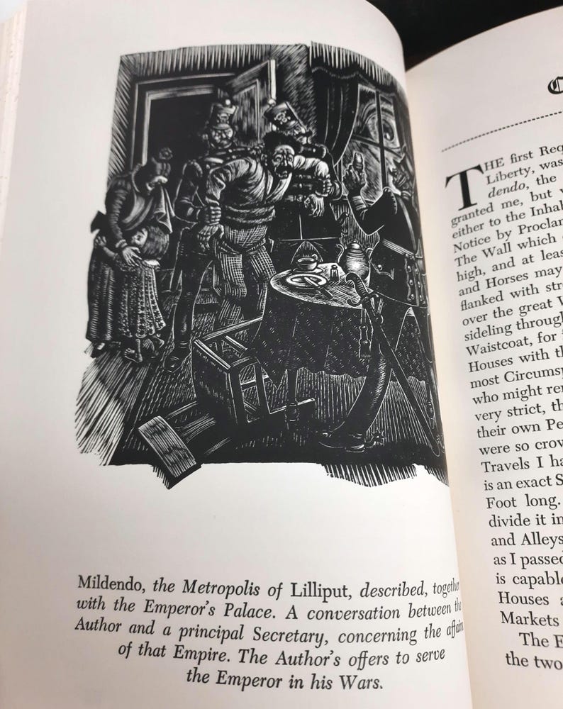 K&ouml;nnte beinhalten: Schwarz-Wei&szlig;-Illustration aus einem Buch, das eine Szene mit mehreren Figuren in historischer Kleidung zeigt, die sich um einen Tisch versammelt haben. Der Text unter dem Bild lautet "Mildendo, die Metropole von Lilliput..." und beschreibt ein Gespr&auml;ch.