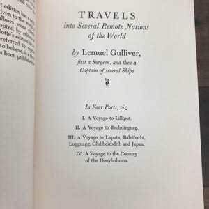 K&ouml;nnte beinhalten: Offene Buchseite mit dem Titel "TRAVELS into Several Remote Nations of the World" von Lemuel Gulliver. Der Text listet die Reisen nach Lilliput, Brobdingnag, Laputa und in das Land der Houyhnhnms auf. Die Seiten des Buches sind cremefarben.
