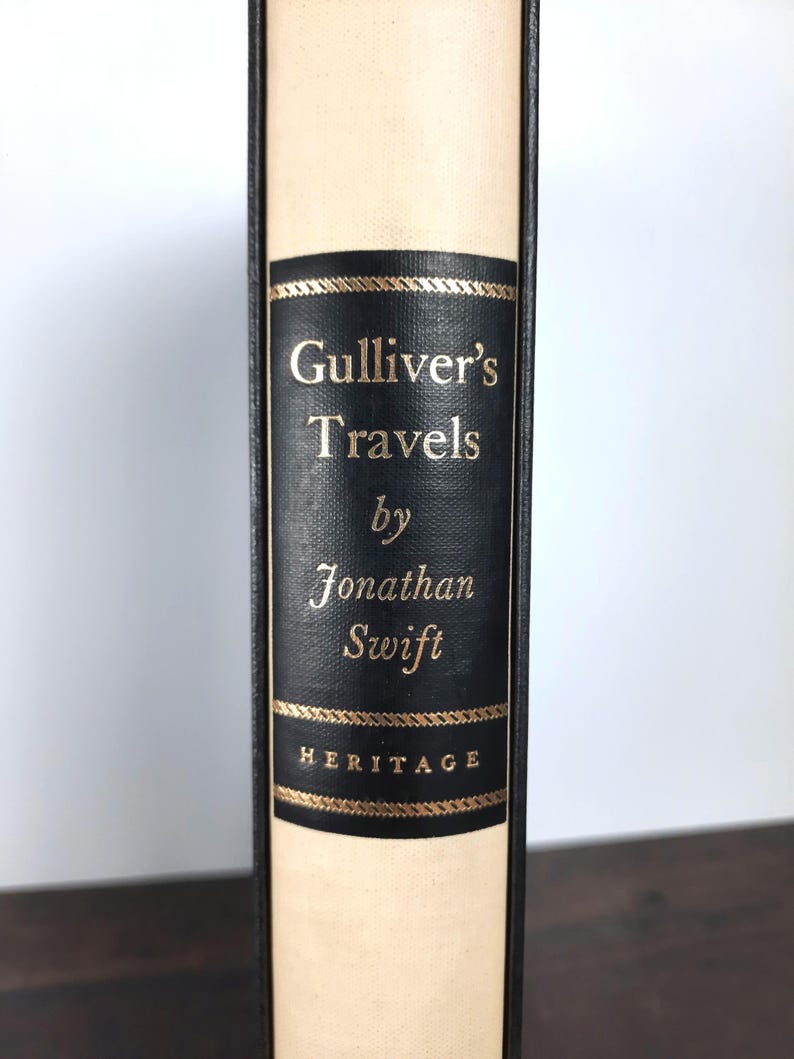 K&ouml;nnte beinhalten: Ein gebundenes Buch mit dem Titel "Gullivers Reisen" von Jonathan Swift. Der Buchr&uuml;cken hat ein schwarzes Etikett mit goldfarbenen Buchstaben und dekorativen goldenen Verzierungen. Das Buch hat einen cremefarbenen Einband und das Wort "HERITAGE" ist unten auf dem Etikett aufgedruckt.
