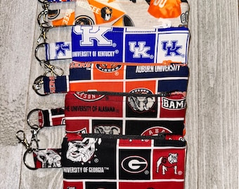 May include: A stack of eight zippered pouches with various college logos and team colors. The pouches are made of fabric and have a zipper closure. The logos include the University of Kentucky, Auburn University, the University of Alabama, and the University of Georgia.