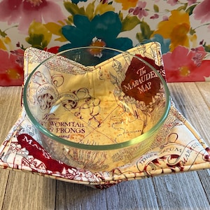 May include: A red and cream-colored fabric bowl cozy with a map design featuring the text "The Marauder's Map".